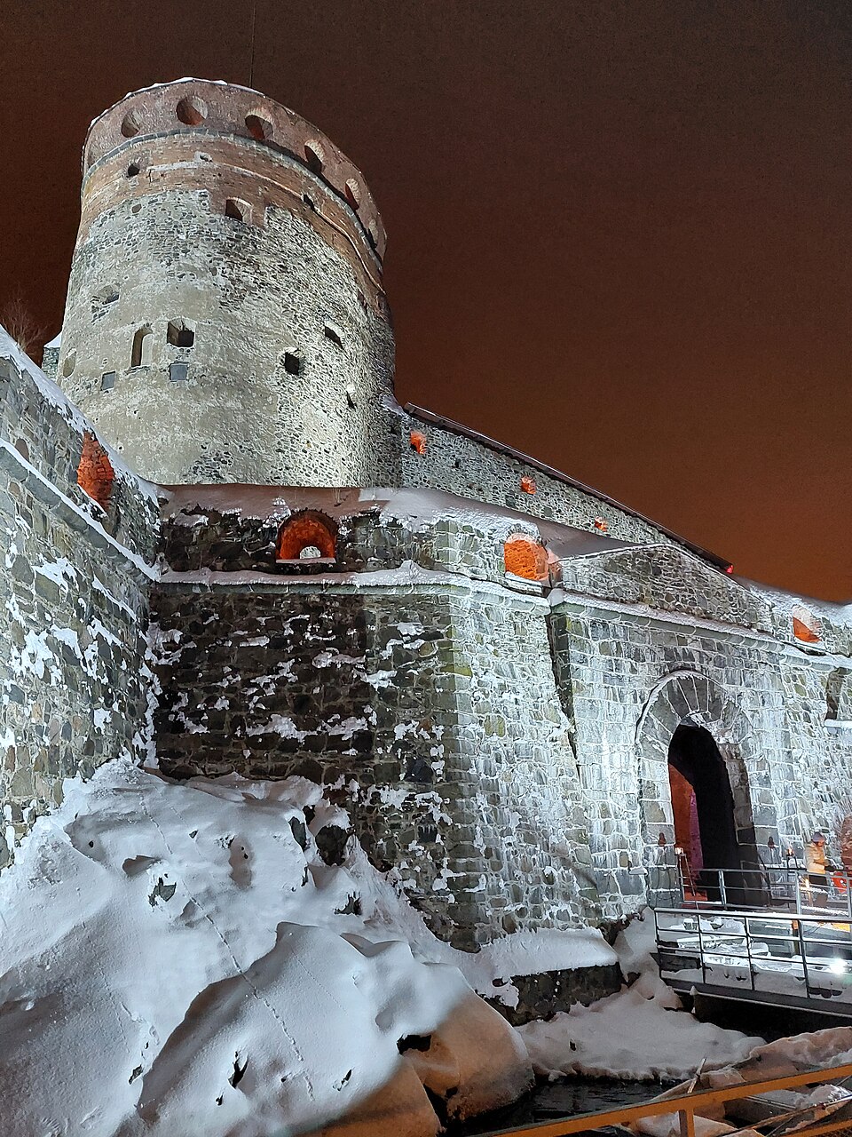 Olavinlinna lit against a winter night — a castle built for legends, and hung with them (photo: Periegetes, CC BY-SA 4.0).